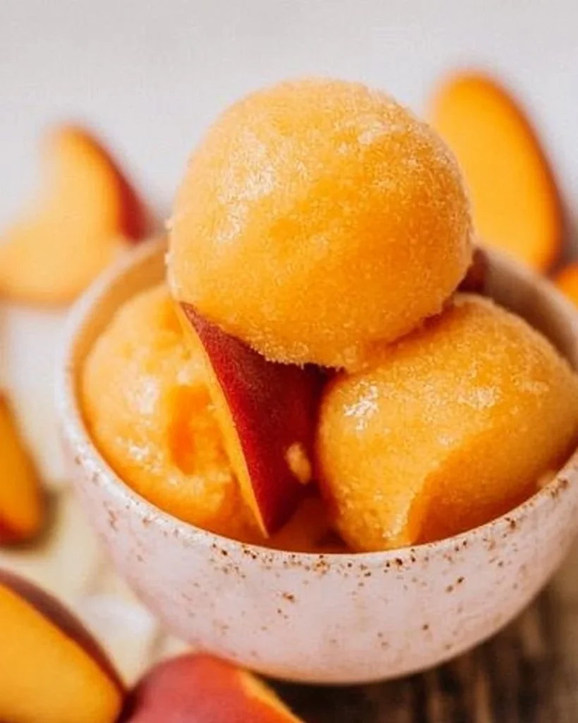 Homemade peach sorbet in a bowl with fresh peach slices